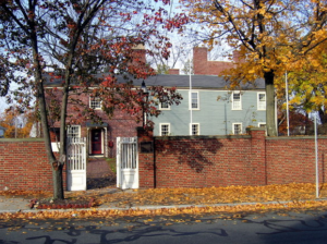 A brick house stands on a street lined with trees in the autumn sky, its window overlooking a road leading to a home in the real estate property.